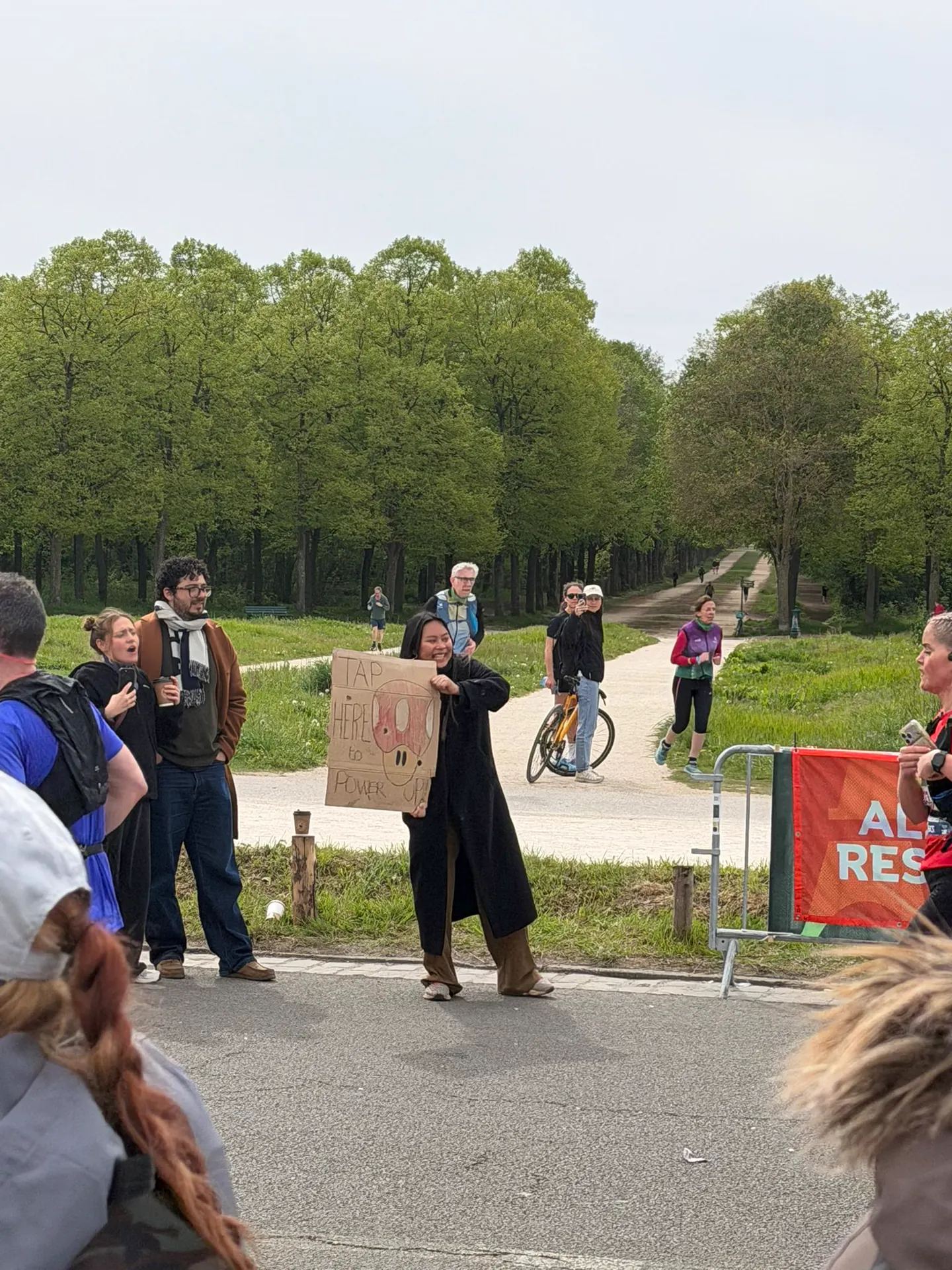Supporter holding a handmade cardboard sign to cheer runners along the tree-lined Paris Marathon route.
