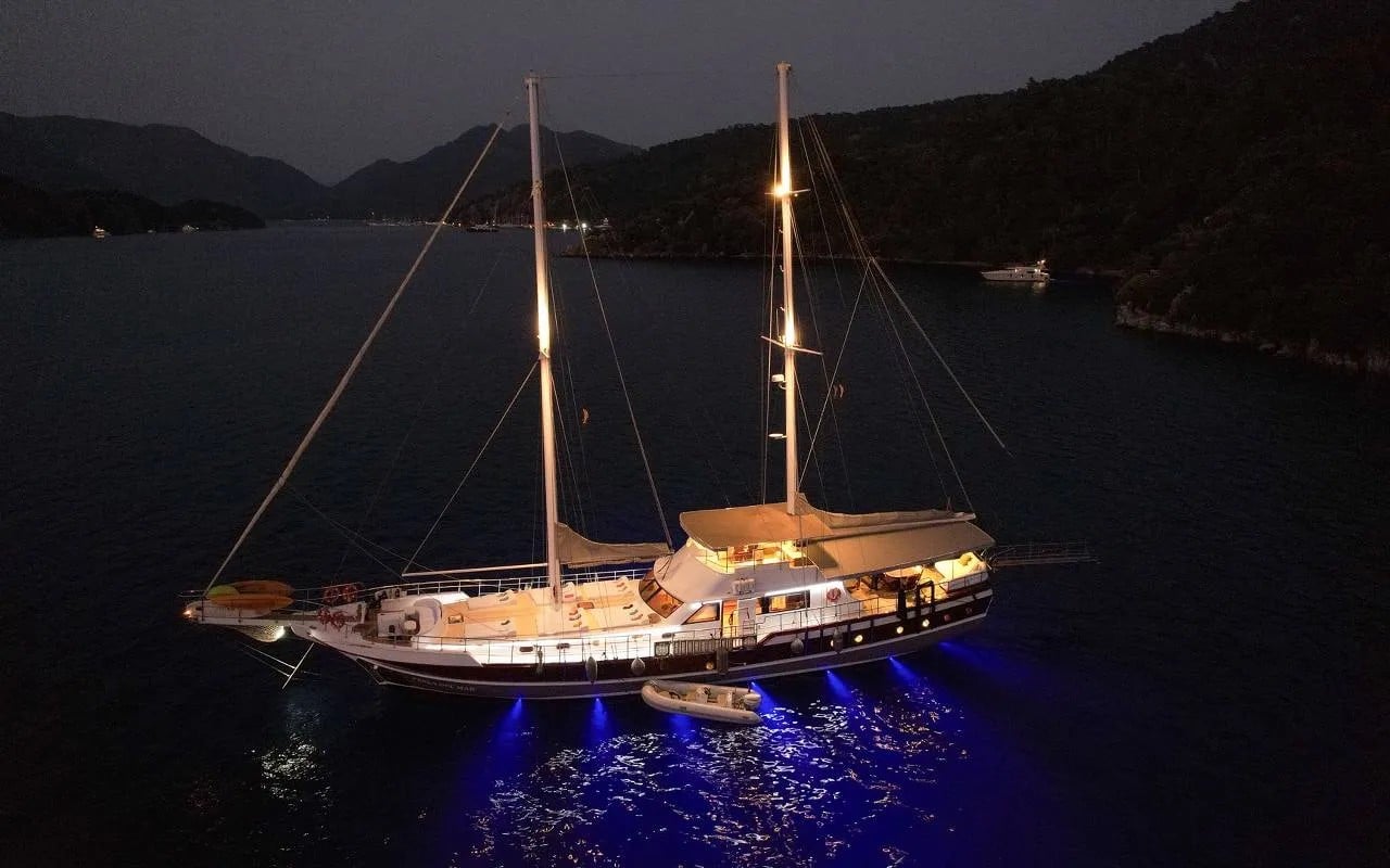Perla del Mar at anchor at night with her underwater lights glowing blue in the water