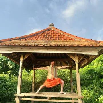 Warrior pose in a tiled roof pavilion surrounded by greenery on the SYB Bali trip