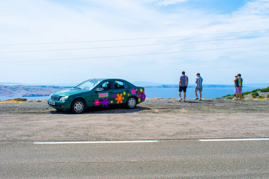 Sticker-covered rally car parked beside a lake on the Hardest Adventures Dash to Dubrovnik.