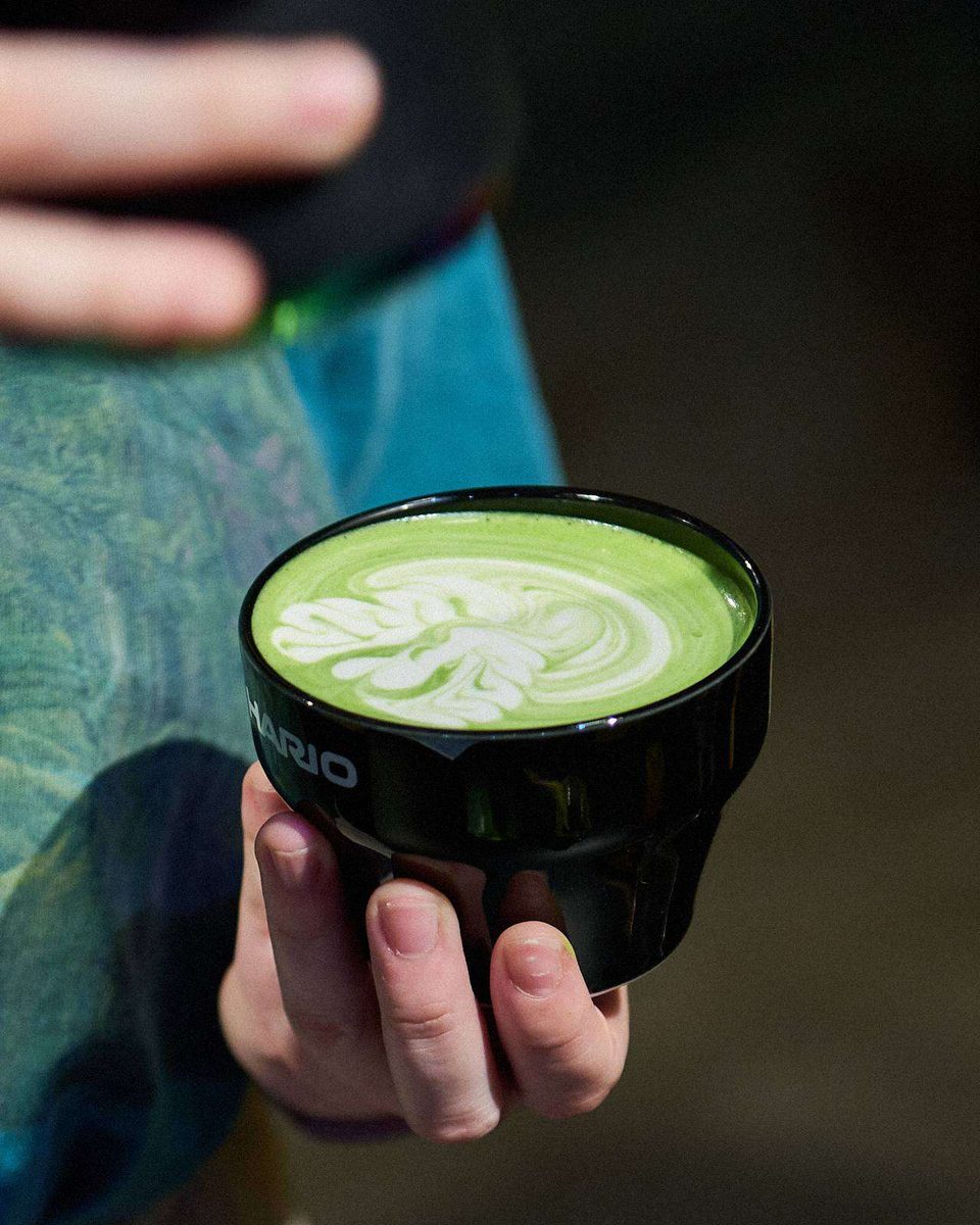 A hand holds up a cup of matcha latte with leaf latte art