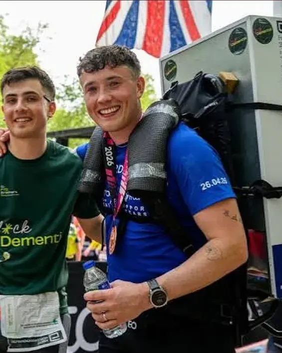 Two runners at a marathon finish, one carrying a fridge on his back