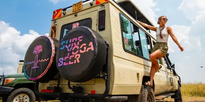 Guest hanging off the side of a safari jeep with Surf Yoga Beer wheel covers in Kenya
