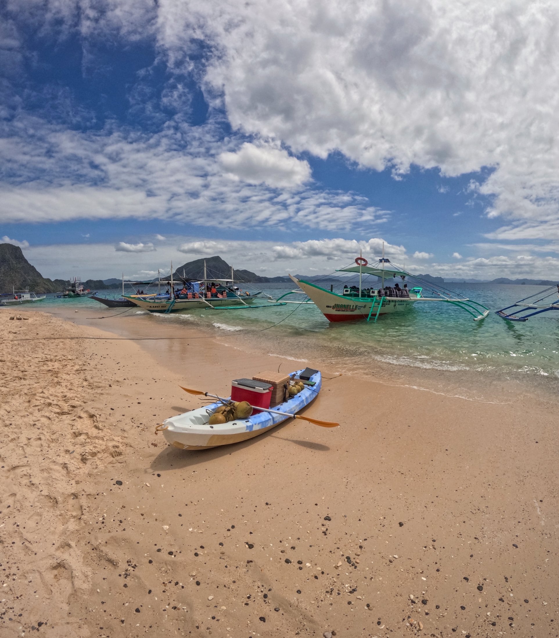 Kayak on the sand with SurfYogaBeer boats anchored in clear water in Palawan