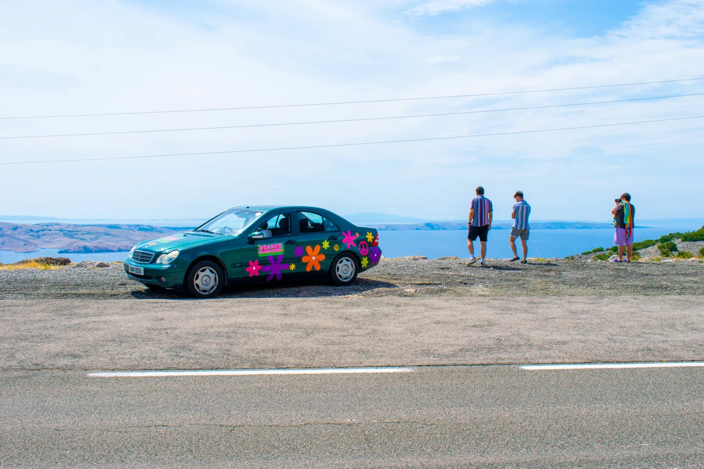 Sticker-covered rally car parked beside a lake on the Hardest Adventures Dash to Dubrovnik.
