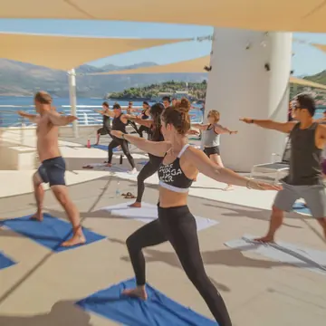 Outdoor yoga class holding warrior pose on a shaded terrace on the SYB Croatia trip