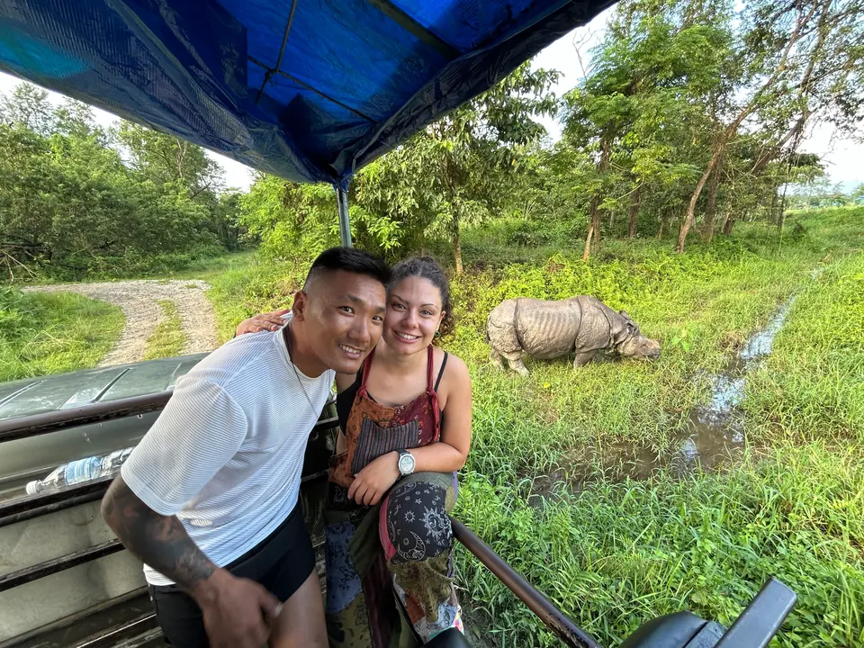 Two travellers on a Chitwan safari, a one-horned rhino grazing behind them