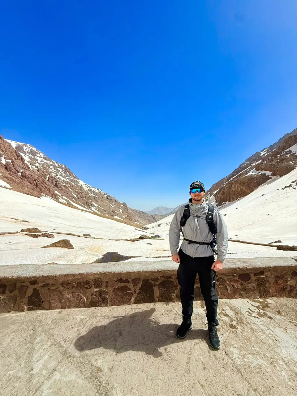 Tom Savage in trekking gear in a snowy mountain valley under a blue sky.