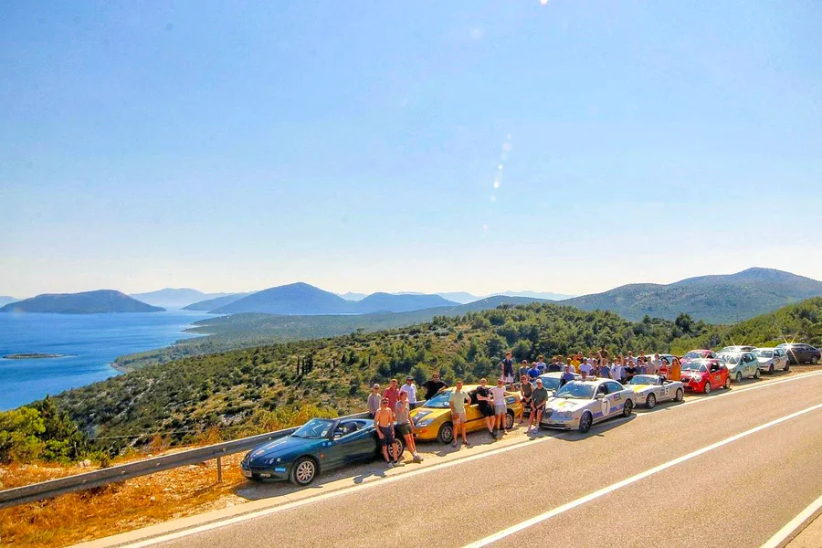 Convoy of sticker-covered cars parked on the Croatian coastal road above the Adriatic on the Dash to Dubrovnik trip