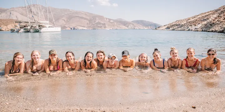 The crew lying in a row in the shallows with catamarans anchored behind on the SYB Greece trip