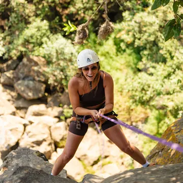 Guest in a helmet smiling while rappelling down a rocky gorge on the SYB Kenya trip
