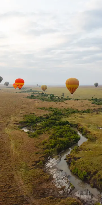 Hot air balloons floating over a winding river and open plains in Kenya