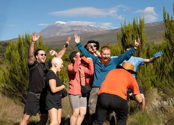 Russ Cook, aka Hardest Geezer, celebrating in front of Mount Kilimanjaro with the group of five strangers he took up Mount Kilimanjaro with Hardest Adventures for free.
