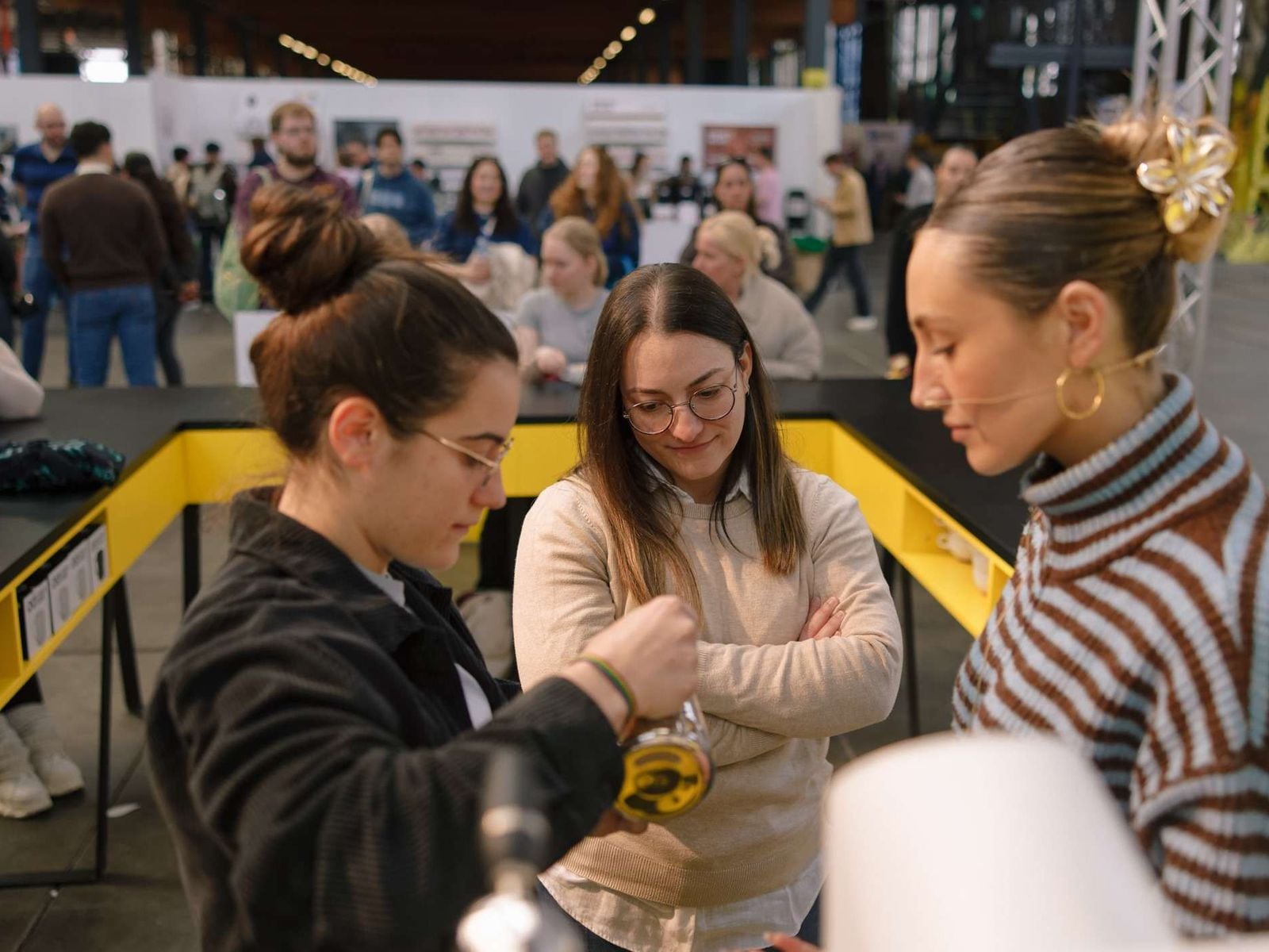 A barista pours steamed milk while two visitors watch closely at a latte art workshop