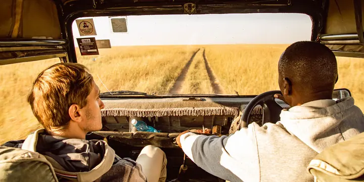 View from inside a safari jeep with the driver heading down a track through golden grass in Kenya