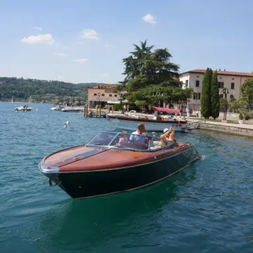 Wooden speedboat cruising past a lakeside village on the SYB Dolomites trip
