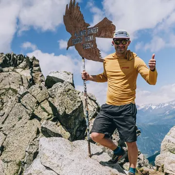 Hiker with a beer and thumbs up beside an eagle sculpture on a summit on the SYB Dolomites trip