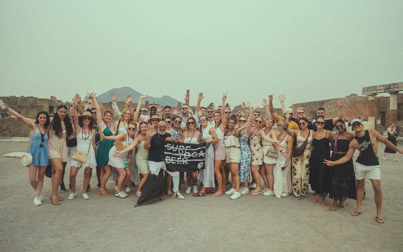 A big SYB group dressed in white cheering with a Surf Yoga Beer flag in Italy
