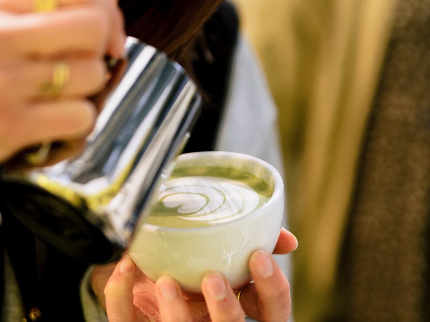 A barista concentrates as she pours latte art into a matcha latte