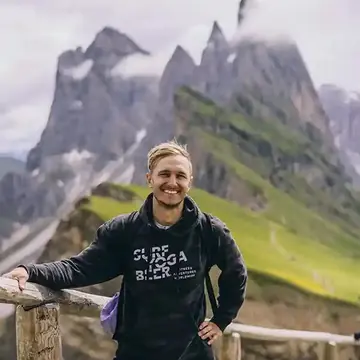 Hiker smiling at a ridge fence with jagged peaks behind on the SYB Dolomites trip