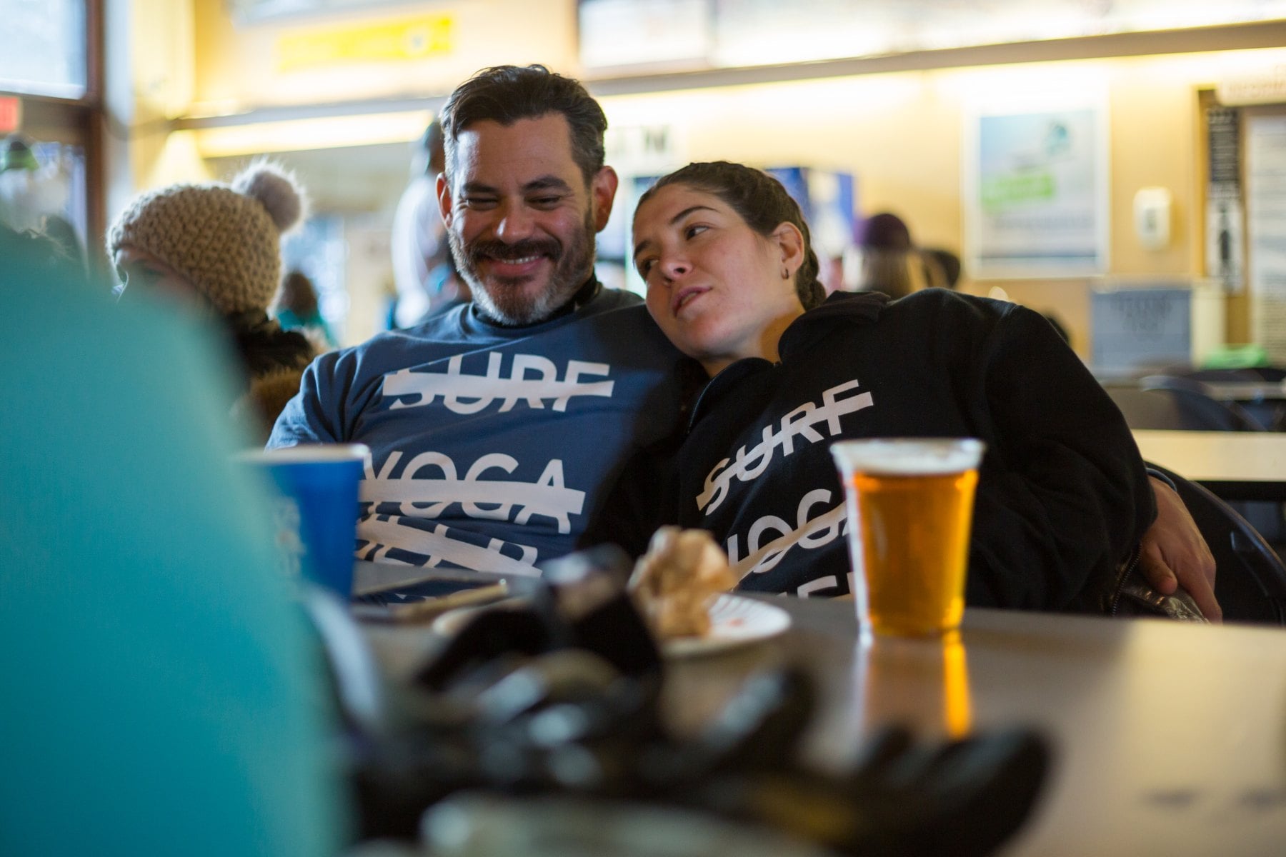 Two SYB crew members at apres in cross-out tops with a beer