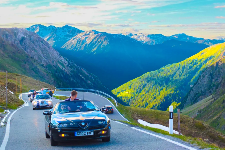 Convoy of cars descending a Stelvio Pass hairpin in the Italian Alps, the most scenic drive on the Dash to Dubrovnik route