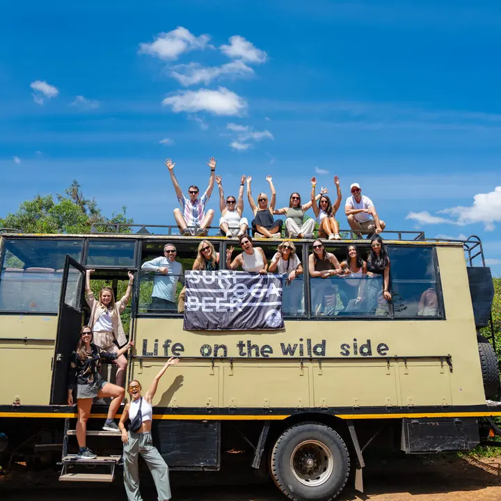 The whole crew cheering from the roof of a safari truck under a blue sky in Kenya