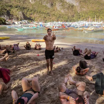 Beach ab workout with the coach in the middle and boats in the bay on the SYB Philippines trip