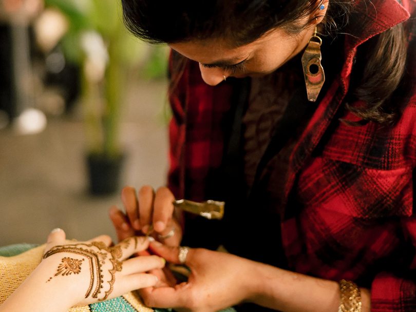 A maker paints an intricate henna design on a visitor’s hand