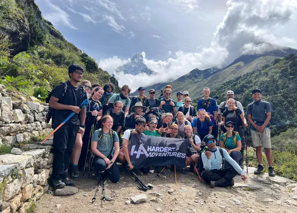 Group of university student hikers on the Hardest Adventures trek to Everest Base Camp posing with a banner in front of clear skies during the best time of year to trek to Everest Base Camp.