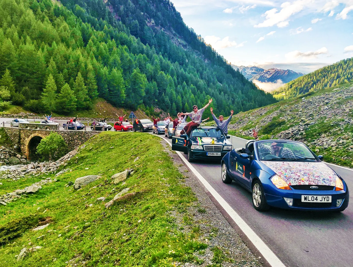 Team cheering beside their sticker-covered car with mountains behind on the Dash to Dubrovnik.
