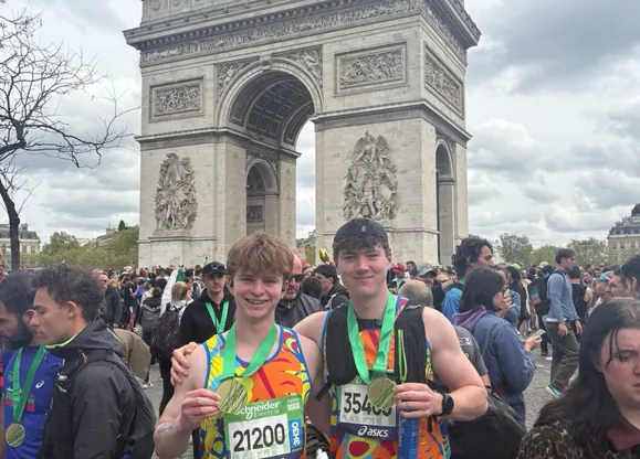 Two male university student runners celebrating with their medals in front of the Arc de Triomphe having just completed the Hardest Adventures Schneider Electric Paris Marathon.