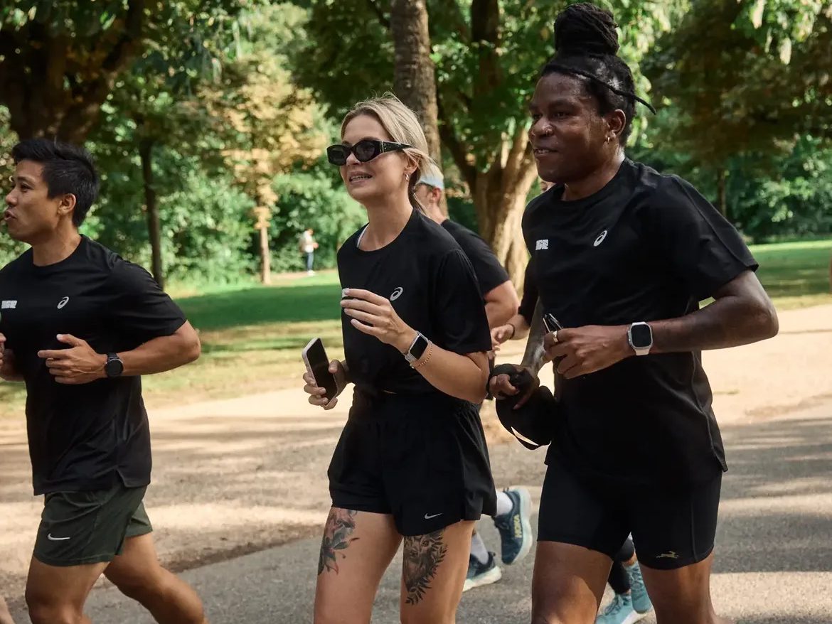 Runners in matching black kit jog together along a tree-lined park path
