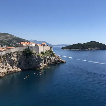 Old city walls on the cliffs above the sea with kayaks passing below on the SYB Croatia trip