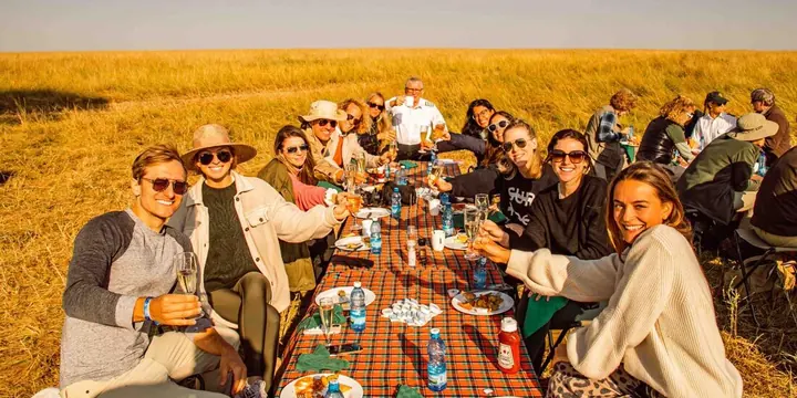 The crew raising glasses at a long table set up in the golden savanna in Kenya