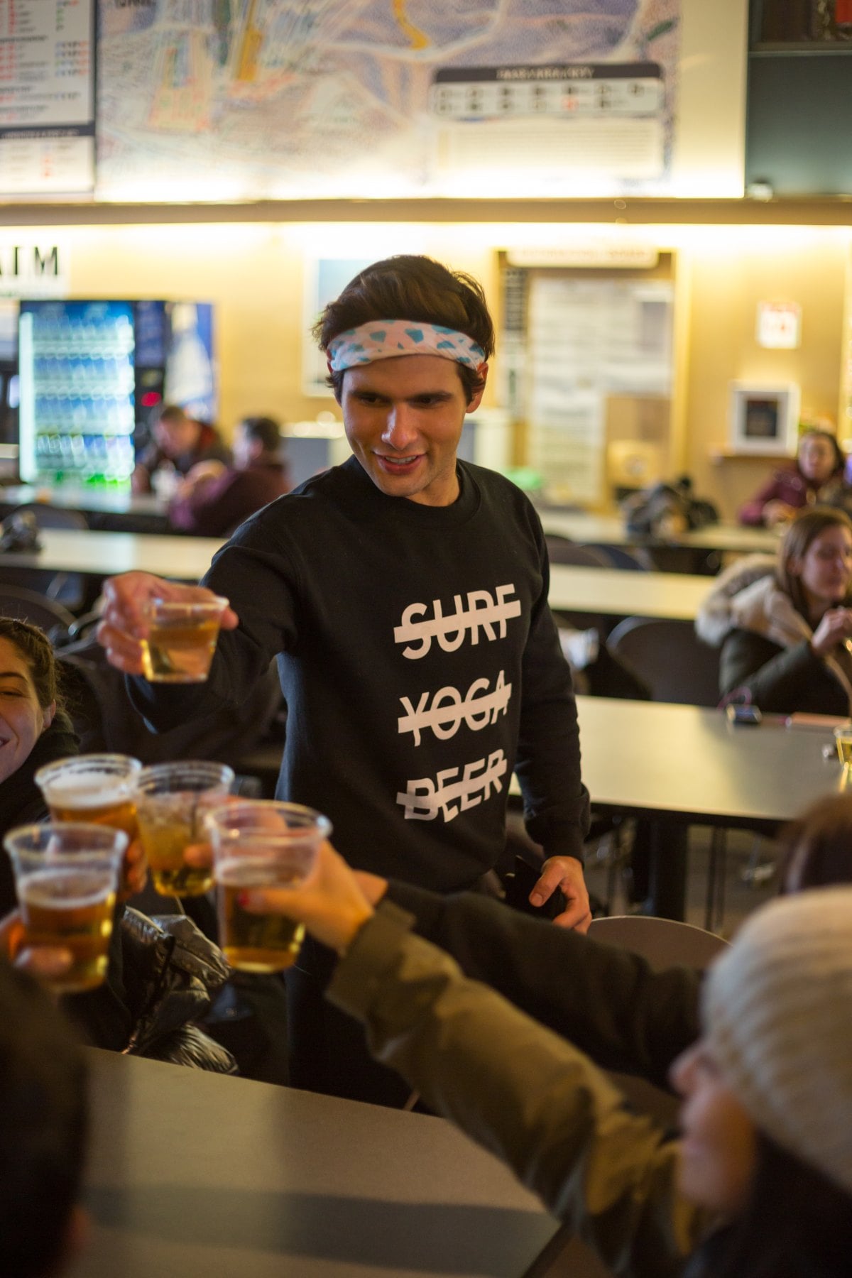 SYB crew member in the black cross-out crewneck raising a beer at apres