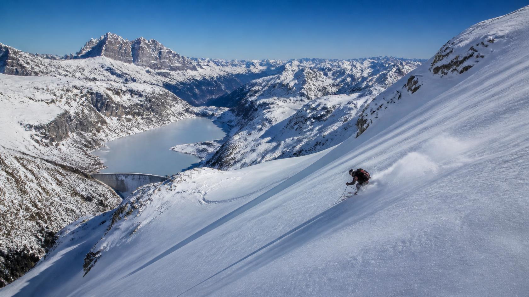 Freeride skier descending a wide glacier slope above a frozen alpine lake