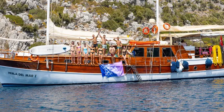 Crew waving from the deck of the wooden gulet anchored below a rocky hillside on the SYB Turkey trip
