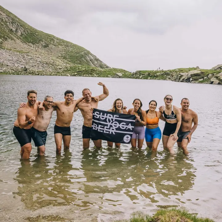 Crew standing in an alpine lake holding the Surf Yoga Beer flag on the SYB Dolomites trip