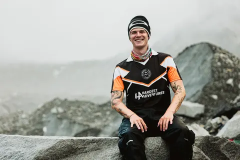 A trekker in a Hardest Adventures jersey on the rock at Everest Base Camp