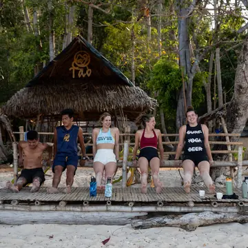 Friends sitting outside a thatched hut at a beach camp on the SYB Philippines trip