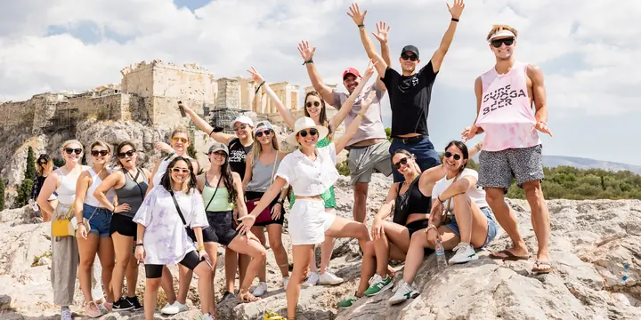 The whole crew with arms up on the rocks below the Acropolis in Athens on the SYB Greece trip
