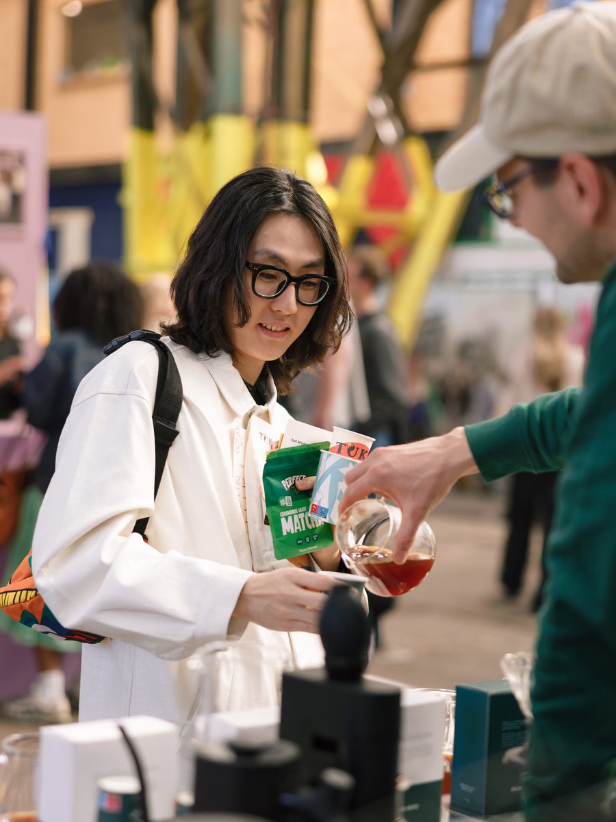 An exhibitor pours a filter coffee for a smiling visitor at their stand