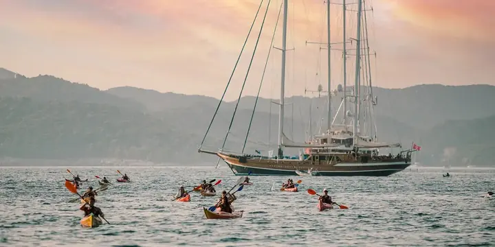 Kayakers paddling past a tall sailing ship under a pink sunset sky on the SYB Croatia trip