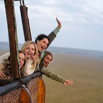 Friends leaning out of a hot air balloon basket high above the plains in Kenya