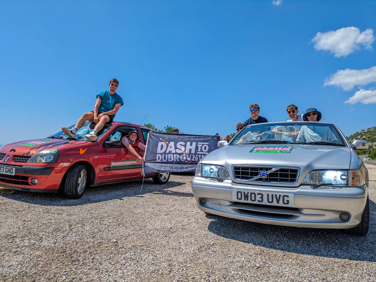 Two rally cars and the team holding a Hardest Adventures banner on the Dash to Dubrovnik.