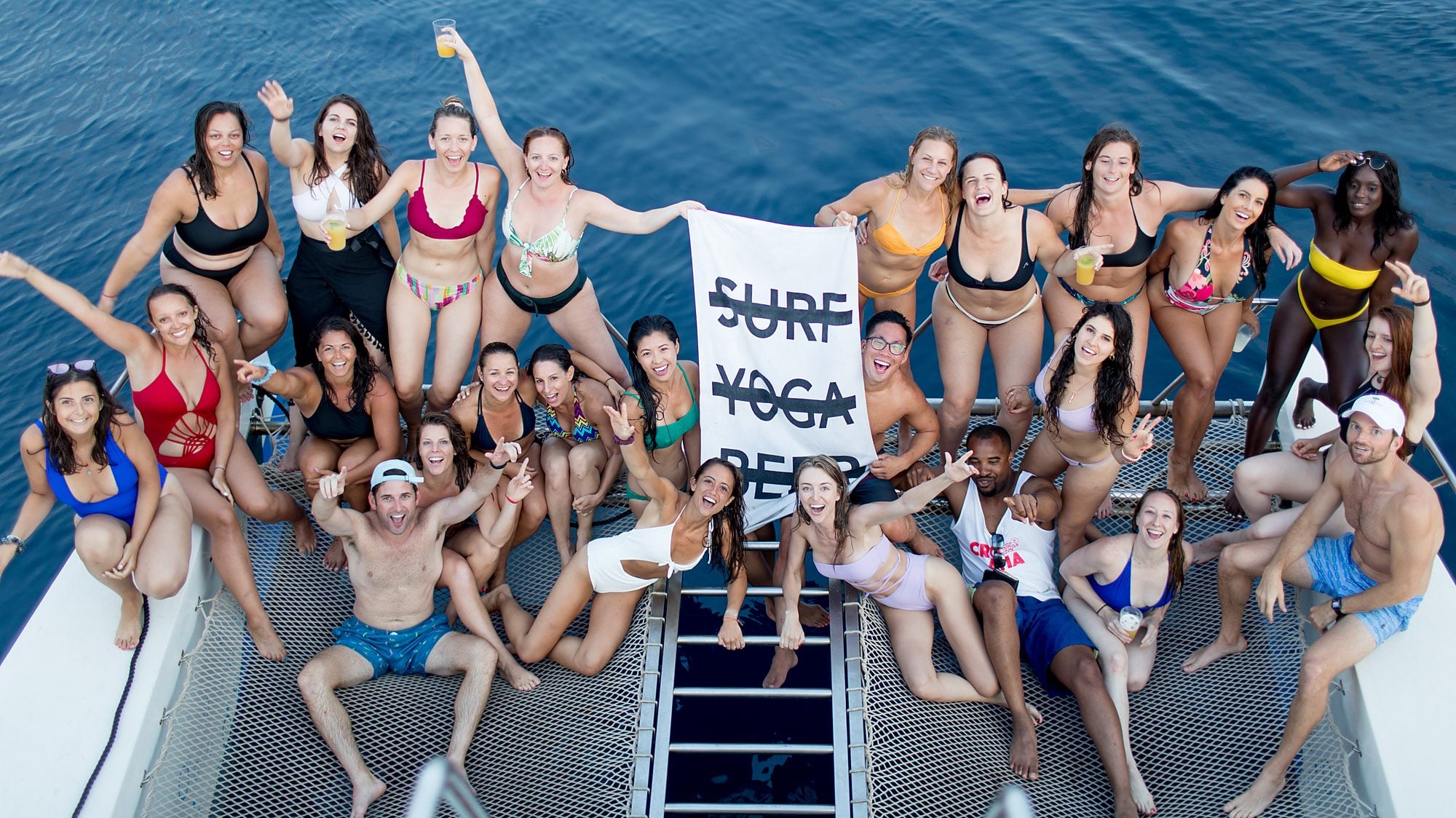 SYB crew on a catamaran in Croatia holding a crossed-out Surf Yoga Beer flag