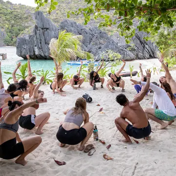 Group workout in a circle on white sand below limestone cliffs on the SYB Philippines trip