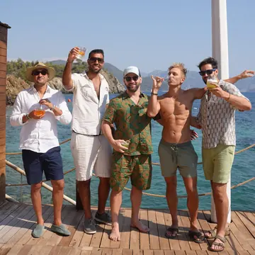 Five guys raising their drinks on a wooden deck by the water on the SYB Turkey trip