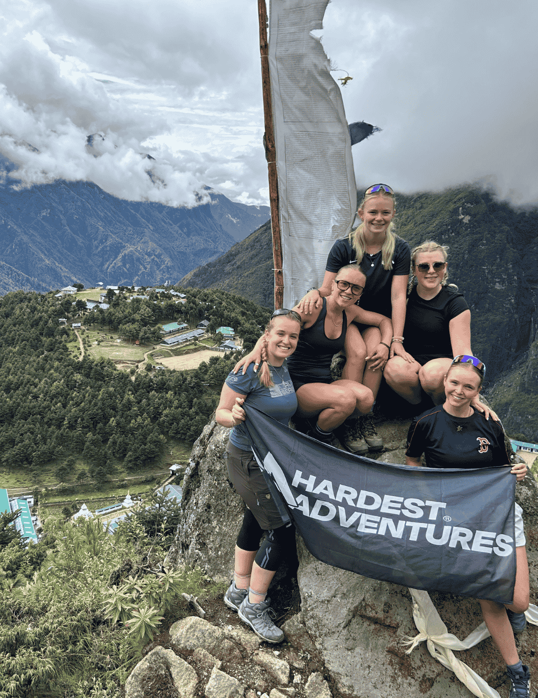 Group of university students celebrating from viewtop of Namche Bazaar waving a Hardest Adventures flag on their way to Everest base camp.